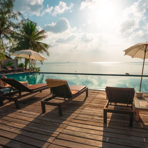 A serene beach scene with sun loungers, umbrellas, and a view of the ocean under a partly cloudy sky at sunset.